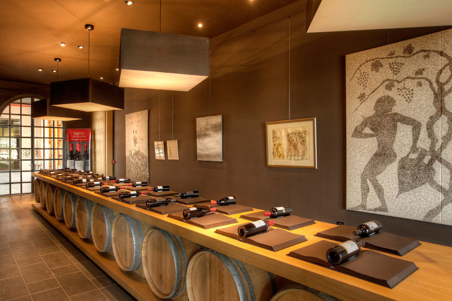 table from wood barells with wine bottles in the background of paintings on the wall of 'Domaine Skouras'